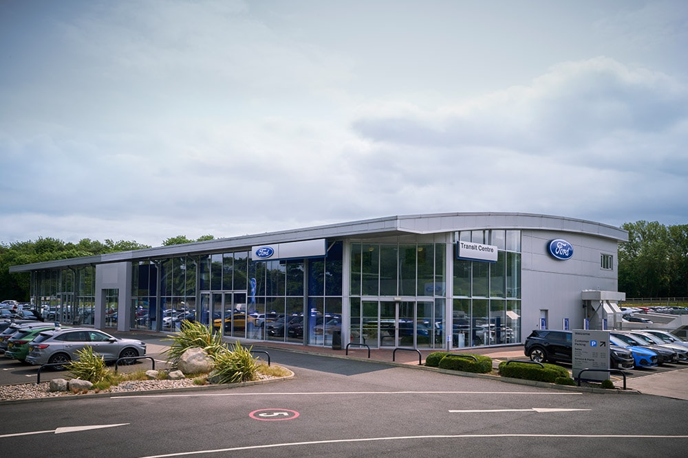 Buitenaanzicht van een modern Ford-dealergebouw met verschillende Ford-voertuigen die buiten geparkeerd staan.