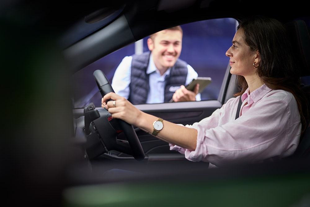 Iemand zit achter het stuur van een Ford-auto, en kijkt naar een monteur die buiten met een tablet staat.