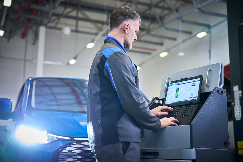 Een techneut die aan een laptop werkt die is aangesloten op een blauwe Ford SUV in een werkplaats.