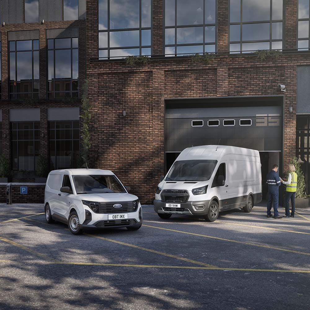 Twee witte Ford-bestelwagens staan geparkeerd voor een modern gebouw, en twee mensen staan te kletsen naast de auto's.