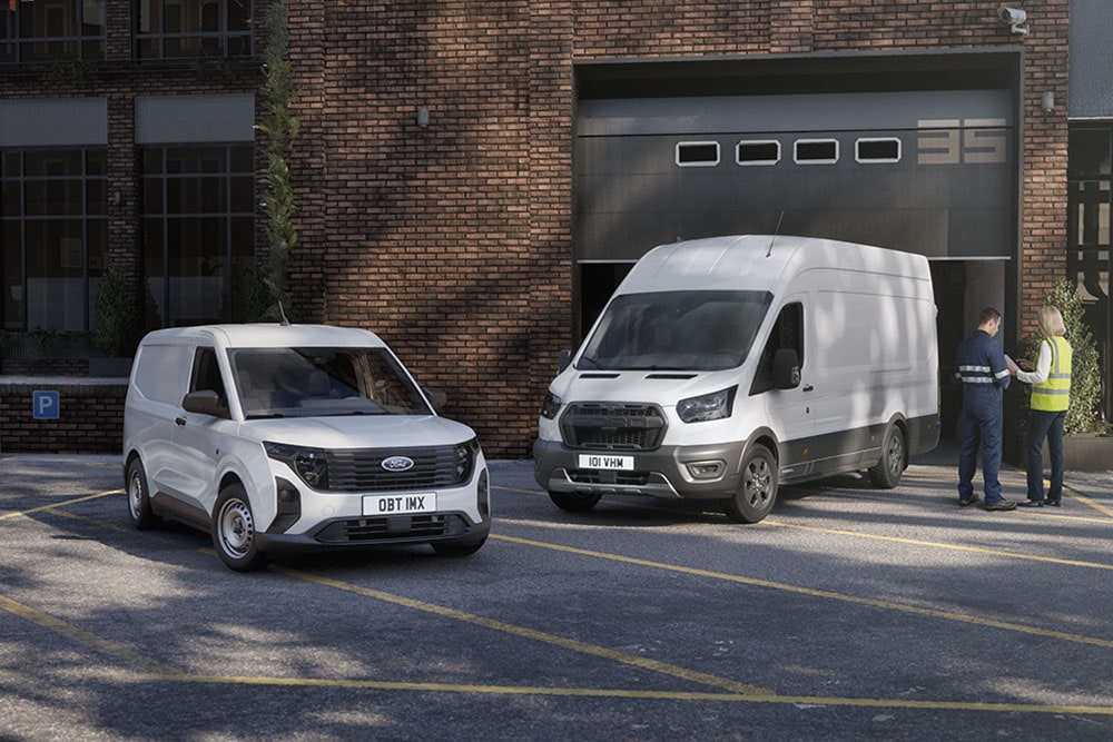 Twee witte Ford-bestelwagens staan geparkeerd voor een modern gebouw, en twee mensen staan te kletsen naast de auto's.