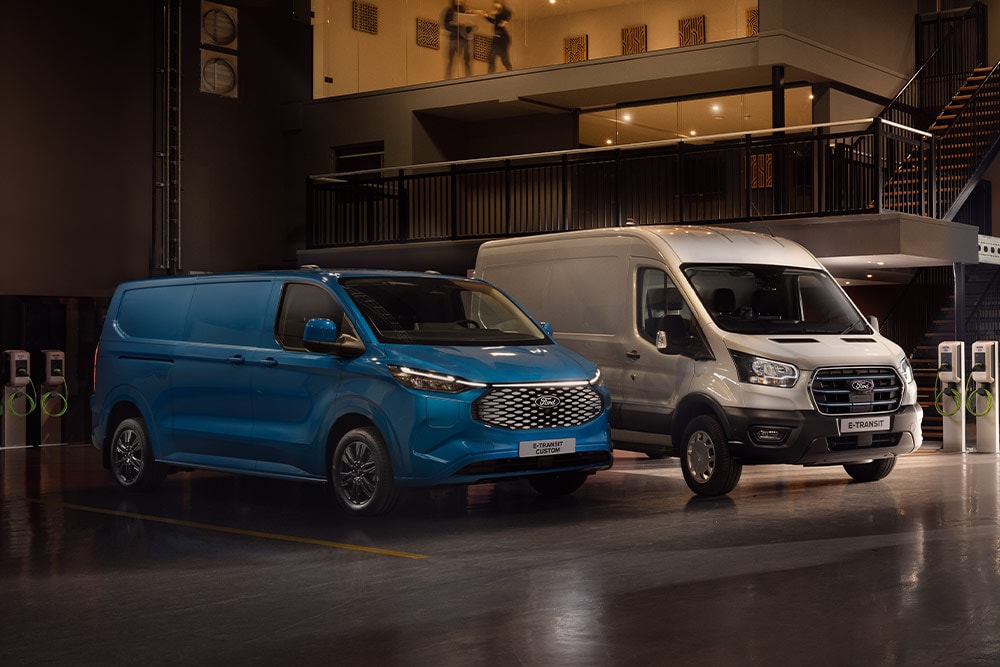 Een blauwe Ford E-Transit Custom en een zilveren Ford E-Transit die worden opgeladen in een parkeergarage.