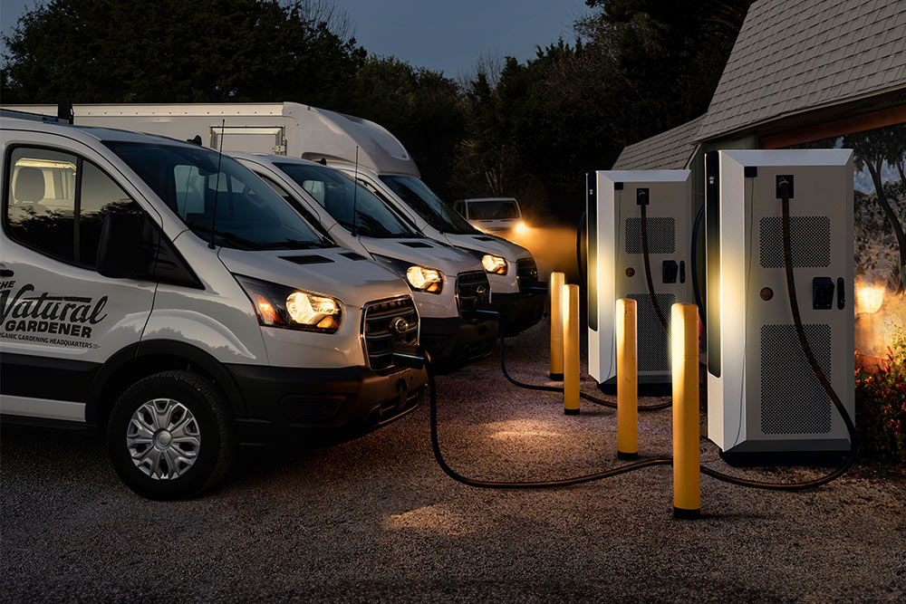 Meerdere witte Ford Transit bestelwagens laden 's nachts op bij elektrische laadstations.