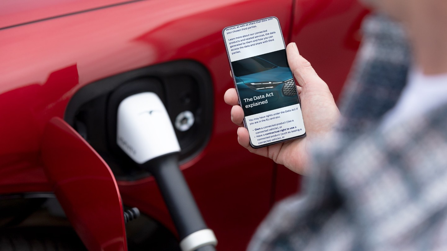 Een persoon die een uitleg over de Europese datawet op zijn telefoon leest naast een oplaadbaar elektrisch voertuig.