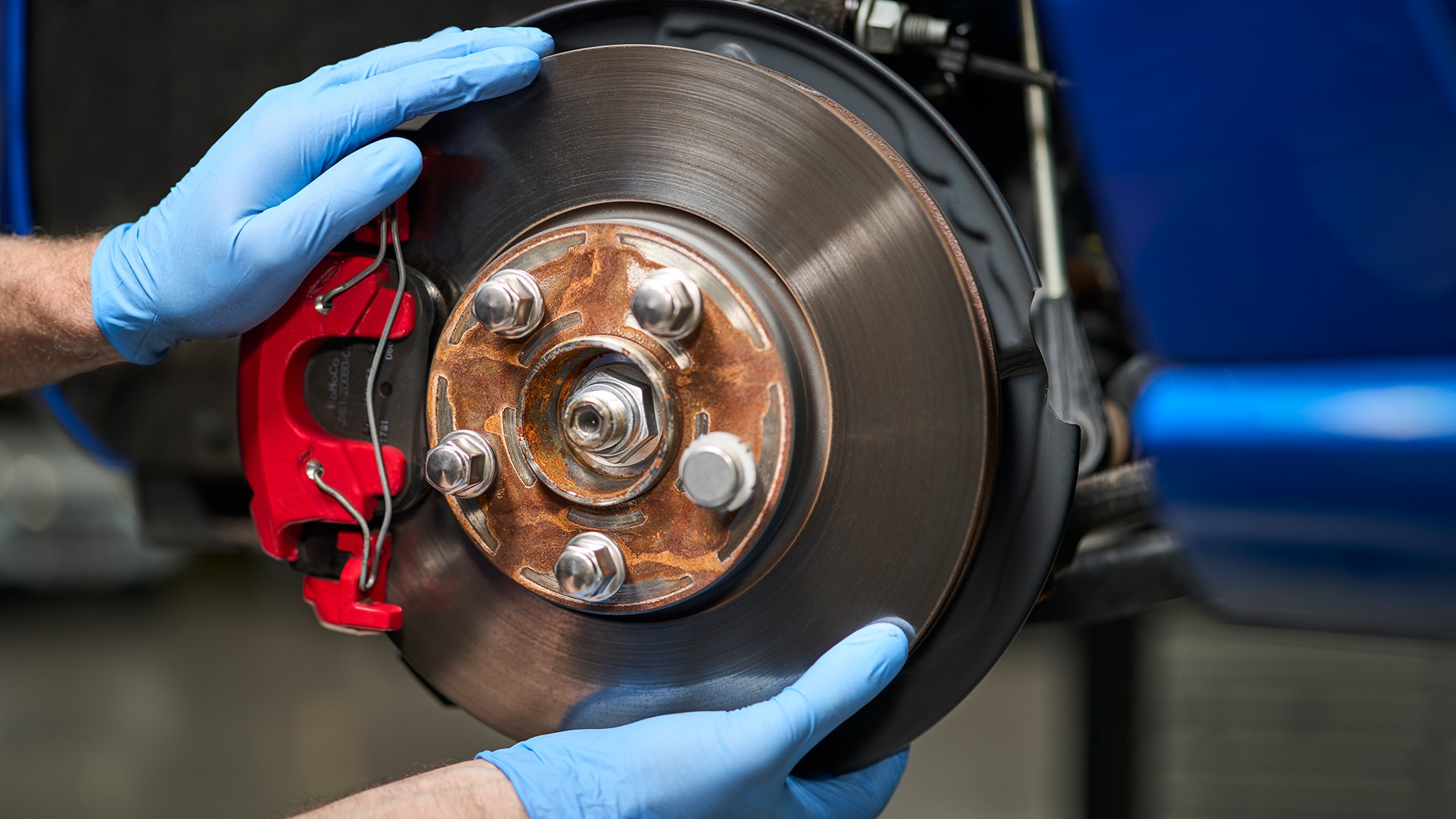 Een monteur met blauwe handschoenen monteert een nieuwe remschijf op een blauwe auto