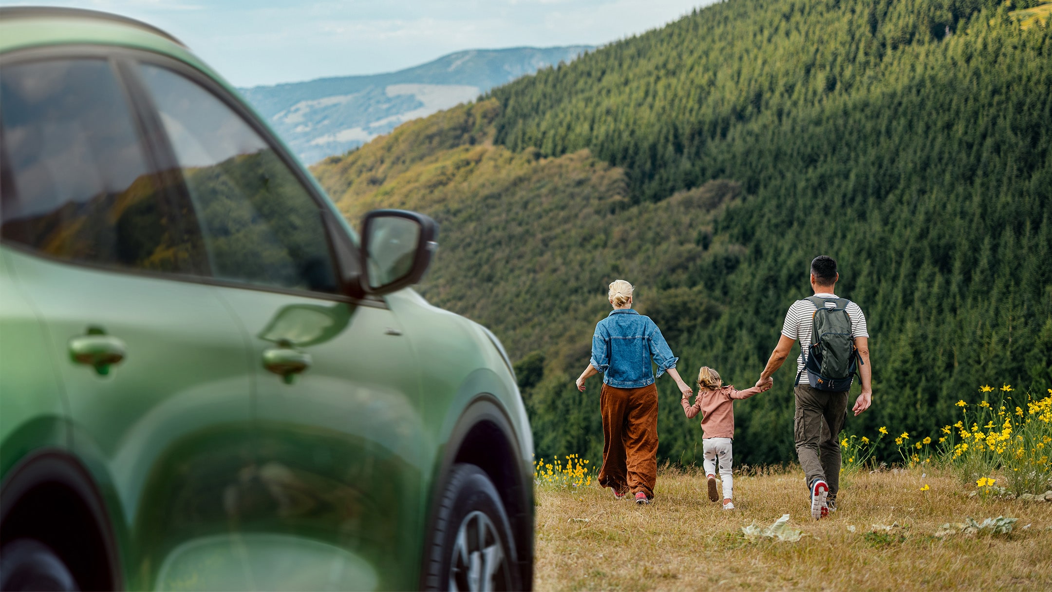 Familie die in een veld loopt naast een groene Ford Kuga.