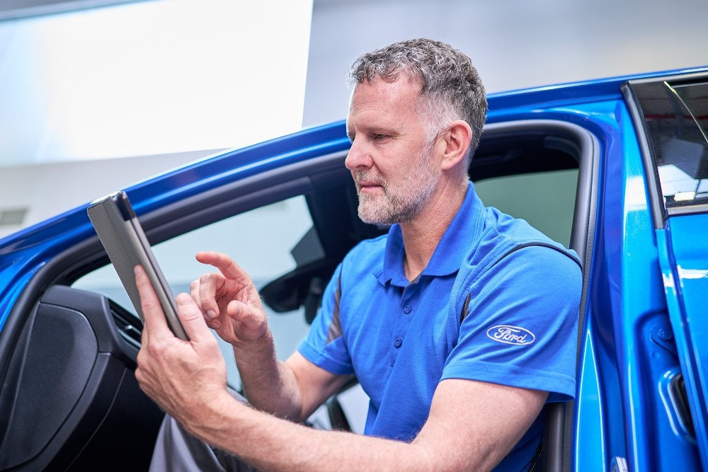 Een Ford-technicus zit in een blauw Ford-voertuig en gebruikt een tablet om voertuigsystemen te controleren.