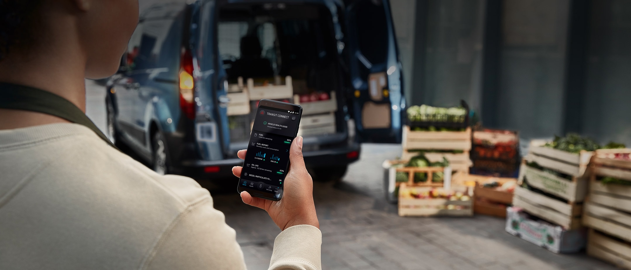 Person checking FordPass on mobile in front of Ford Van and wooden crates with goods